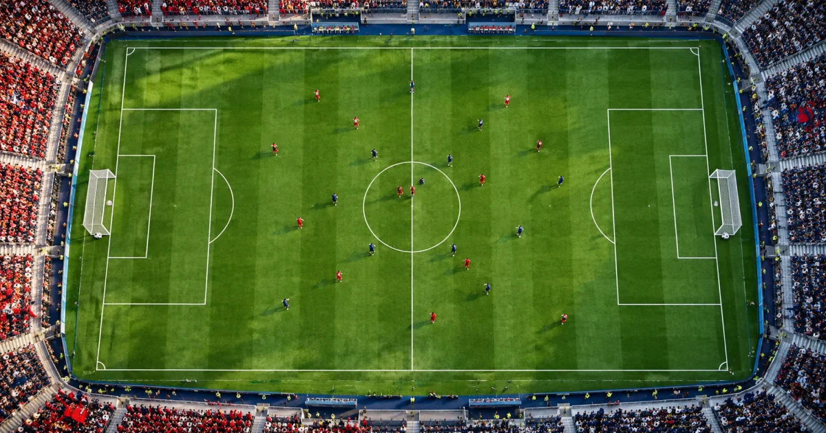 Campo visto de cima com uma bola em cada baliza e jogadores fictícios no meio-campo.